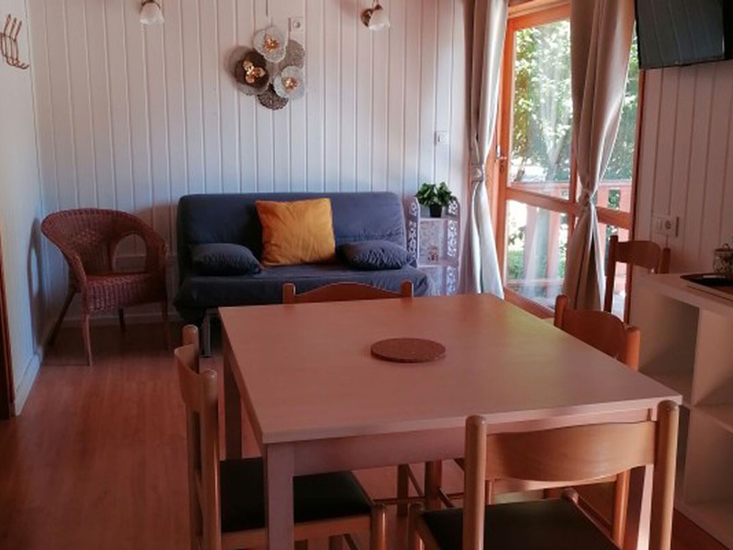 Une pièce chaleureuse avec une table à manger en bois, un canapé avec des coussins, un fauteuil en osier et une fenêtre avec des rideaux.
