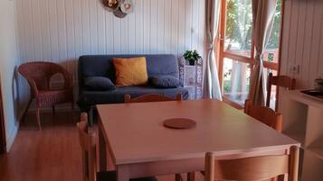Une pièce chaleureuse avec une table à manger en bois, un canapé avec des coussins, un fauteuil en osier et une fenêtre avec des rideaux.