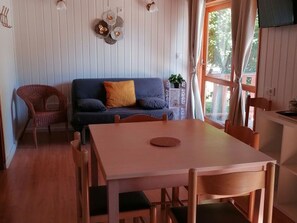 Une pièce chaleureuse avec une table à manger en bois, un canapé avec des coussins, un fauteuil en osier et une fenêtre avec des rideaux.
