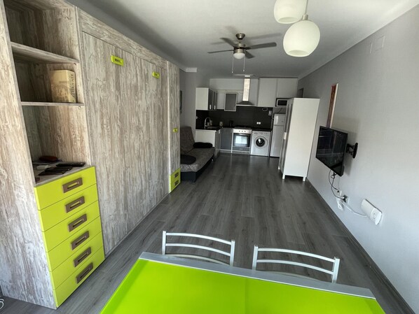 A compact kitchen with a dining area, a ceiling fan, and a built-in washing machine. - Downtown Roses Studio, 100m from Beach, Private Parking Included (Roses)