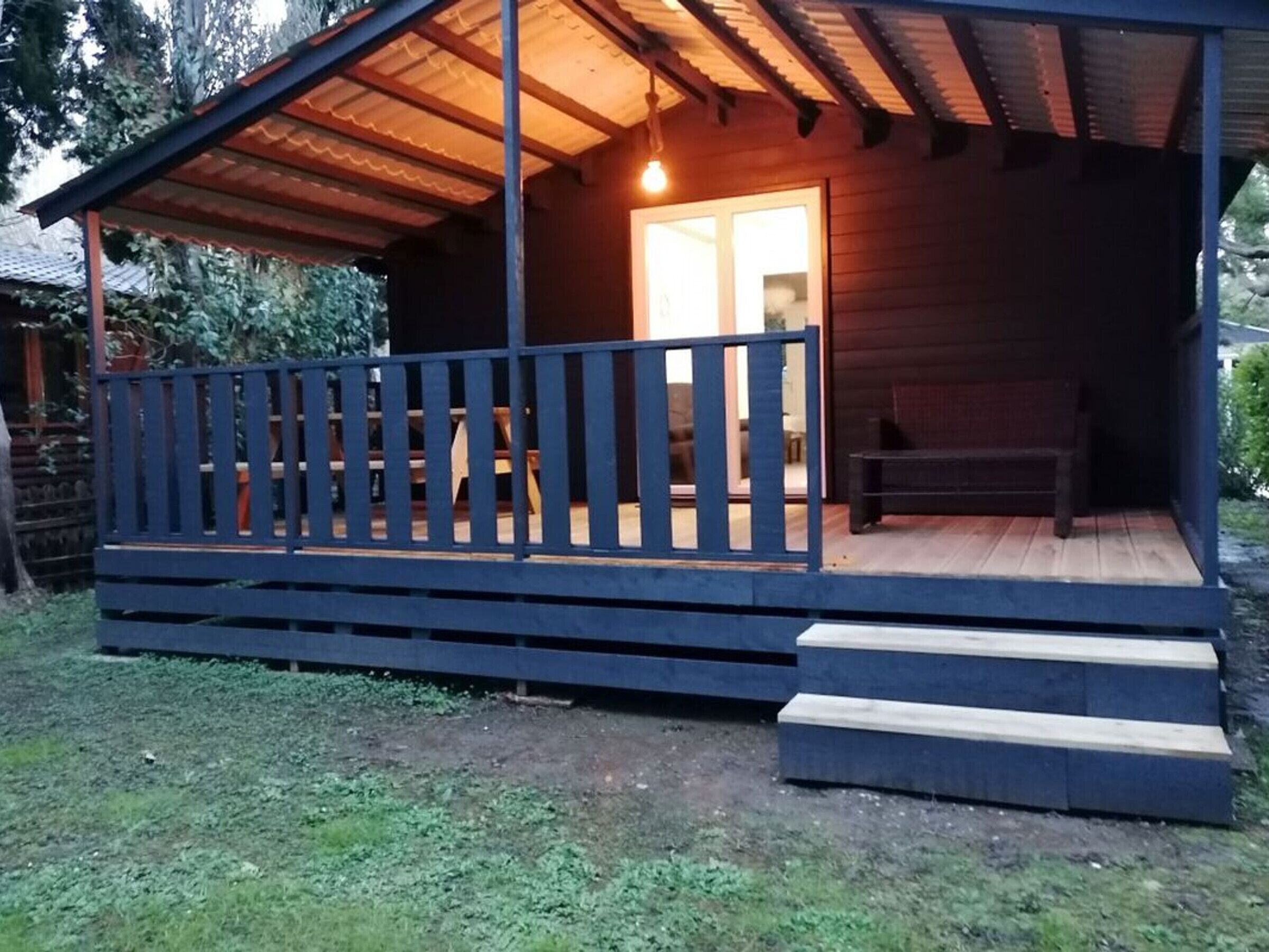 Une cabane en bois avec une véranda, des marches et un banc.
