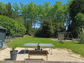 Une terrasse avec une table et un banc, entourée d’une pelouse et d’arbres.