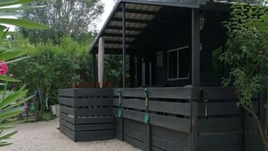 A covered outdoor area with a gravel floor, surrounded by greenery and a wooden fence. - Chalet air-conditioned pets welcome - 5 guests (Noves)