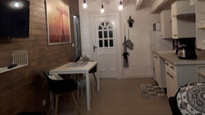 A modern kitchen with a dining area, wooden walls, a white door, and hanging lights.