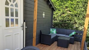 A covered outdoor seating area with a white door, dark wooden walls, and a wooden deck.