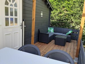 A covered outdoor seating area with a white door, dark wooden walls, and a wooden deck. - Chalet with AC - 2 guests (Noves)
