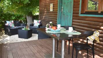 Une cabane en bois dotée d’une terrasse, de meubles de jardin et d’une table dressée pour deux personnes.