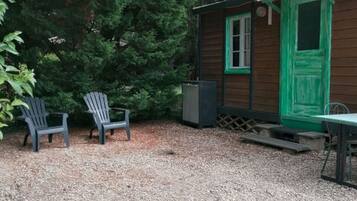 Une cabane avec un sol recouvert de gravier, deux fauteuils Adirondack, une table et une porte verte.