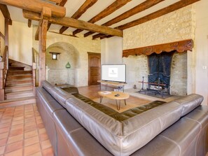 A spacious living area with a stone fireplace, leather seating, and a television on a wooden stand.