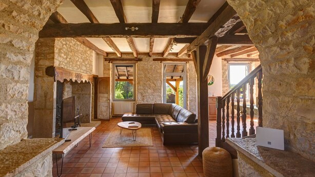 A rustic stone-walled room with a wooden ceiling, a sofa, a small table, and a bench.