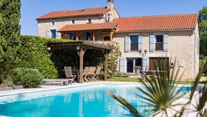 A stone building with a swimming pool, outdoor seating, and a pergola.