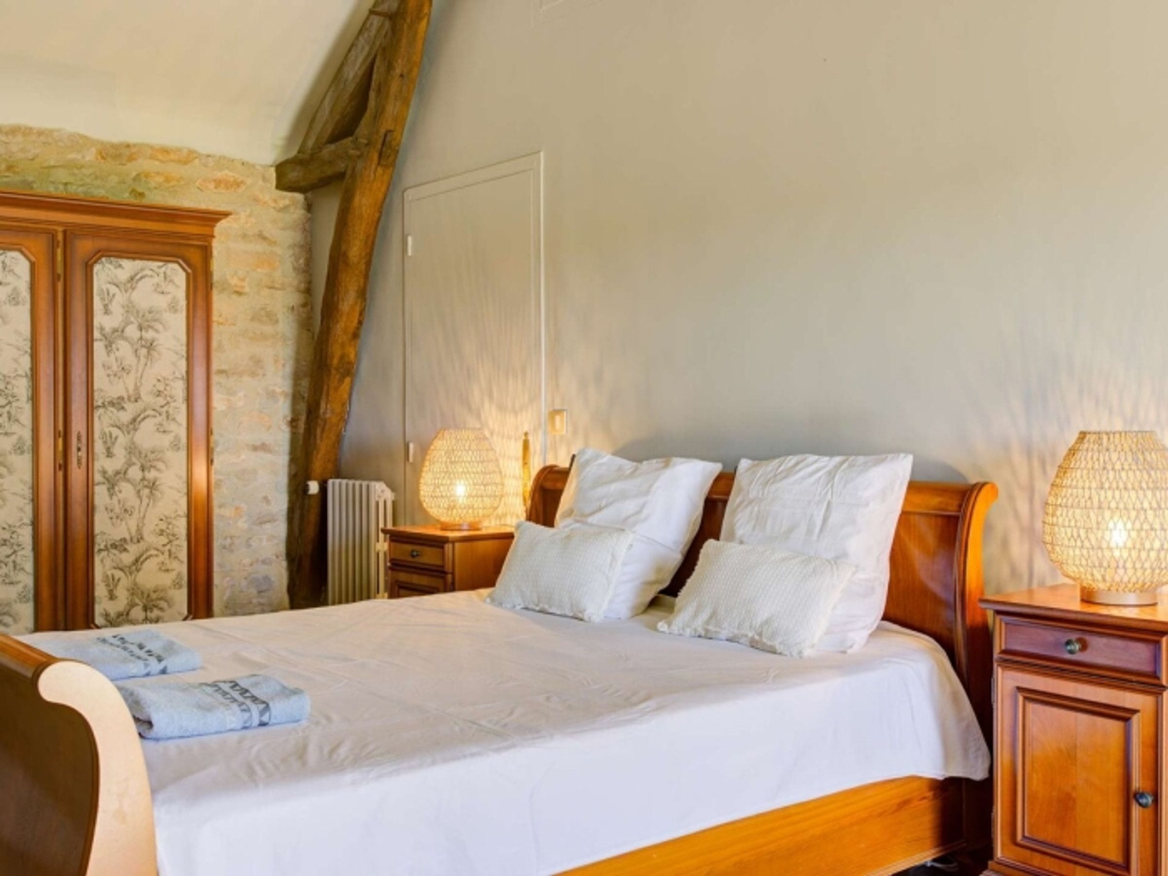 Ein Schlafzimmer mit einem hölzernen Bett, weißen Leinen, zwei Nachttischlampen und einer Steinwand.