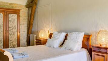 Ein Schlafzimmer mit einem hölzernen Bett, weißen Leinen, zwei Nachttischlampen und einer Steinwand.