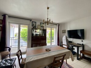 Un espace repas comprenant une table, des chaises, un lustre, un téléviseur et une vue à travers la porte vitrée.