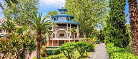 Un bâtiment de style traditionnel, avec un toit bleu, entouré d’une végétation luxuriante et bordé d’un sentier.