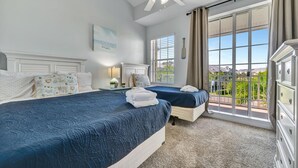 Quarto de hotel com duas camas, um ventilador de teto, uma janela grande com vista e uma cômoda.