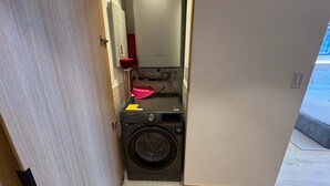 Une petite buanderie équipée d’un lave-linge, d’un évier rouge et d’un chauffe-eau.