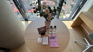 Un espace de bureau moderne doté d’une grande fenêtre, d’une table en bois, d’un vase avec des fleurs, d’une carte de bienvenue, d’une carte contenant des conseils et de deux bouteilles d’eau.