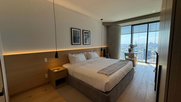 Ein modernes Schlafzimmer mit einem großen Bett, Nachttischen, Blick auf die Stadt und gerahmten Kunstwerken an der Wand.