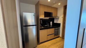 Eine kompakte Küche mit Edelstahl-Kühlschrank, Mikrowelle, Spüle und Holzschränken.