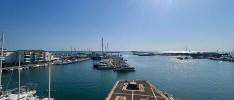 Una marina con barcos amarrados, cielo despejado y sol brillante.