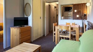 Kompakti hotellihuone, jossa on televisio, puuhuonekalut, ruokailutila ja pieni keittiö.