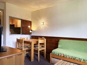 A room with a wooden table and chairs, a green sofa, a wooden cabinet with a mirror, and a wall-mounted light fixture. - Spacious studio with WiFi, view - 4-5 guests (Les Orres)