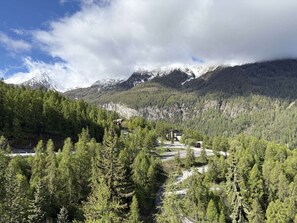 A mountainous landscape with a forested valley, a winding road, and a building with a distinct architectural style. - Spacious studio with WiFi, view - 4-5 guests (Les Orres)