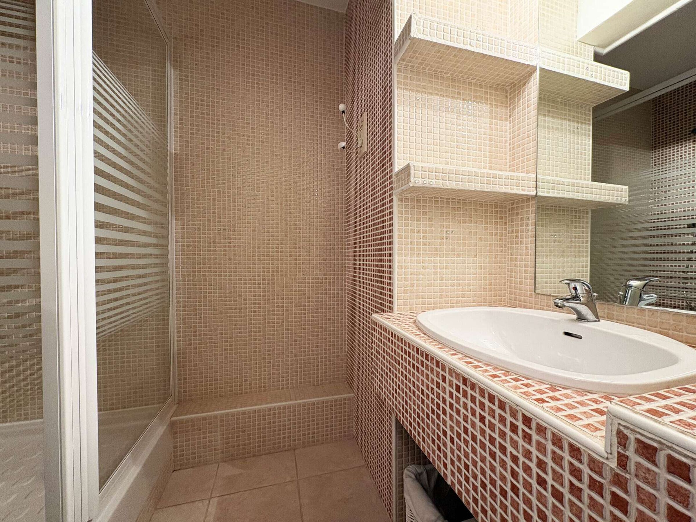 Een badkamer met een douche, wastafel en spiegel.