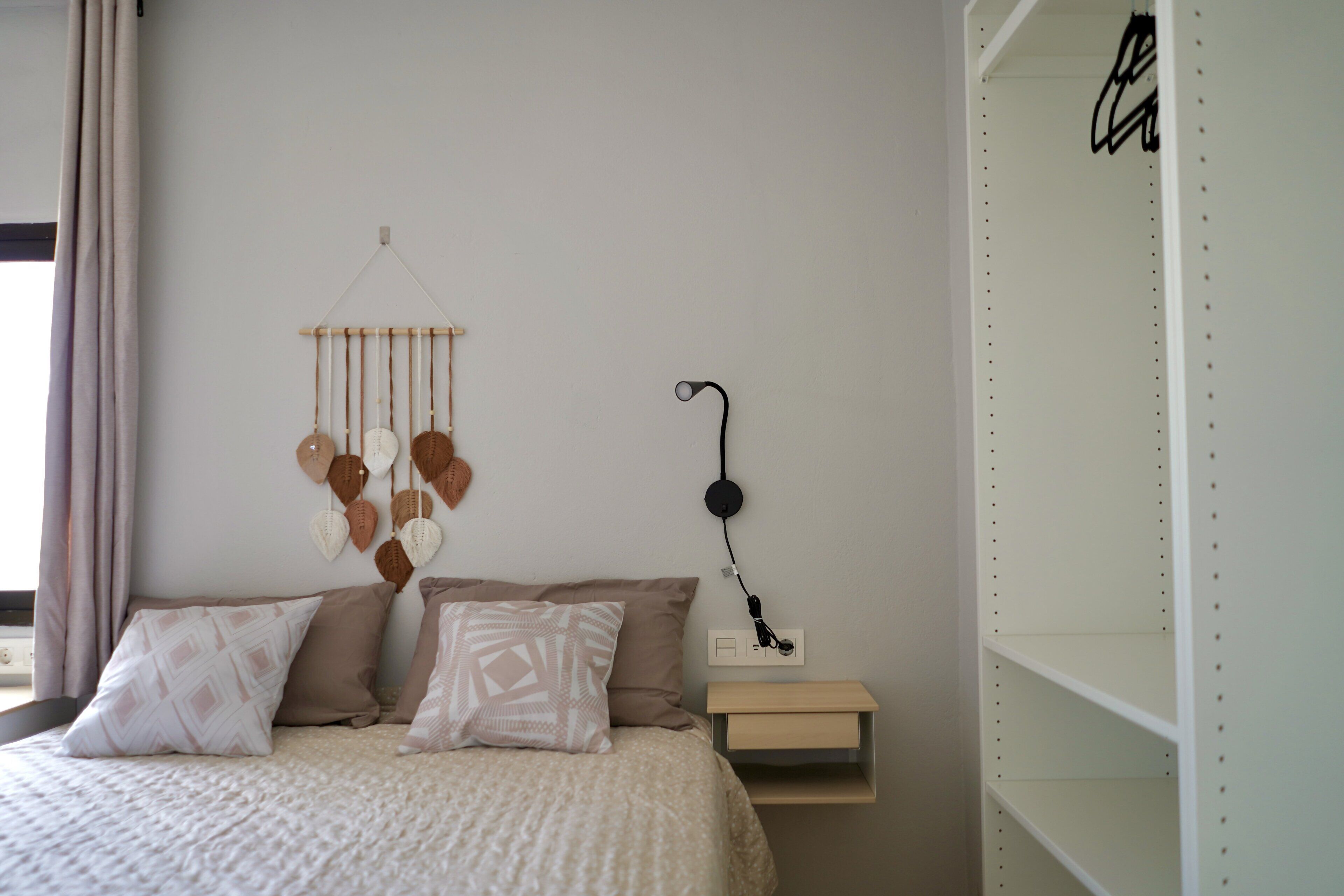 Un dormitorio con cama, almohadas, mesita de noche, decoración en la pared y una estantería.