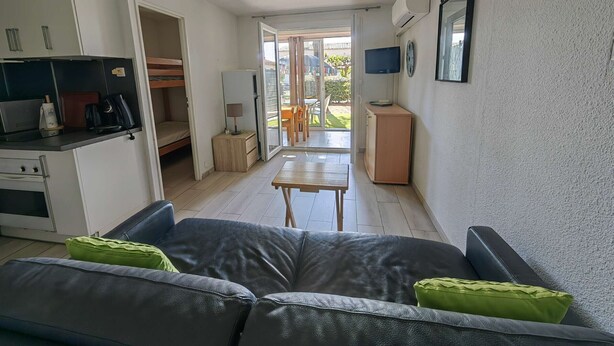 A compact living space with a kitchenette, a sofa, a dining table, and a view of the outdoors. - Studio cabin, secure parking - 4 guests (Cap d'Agde)