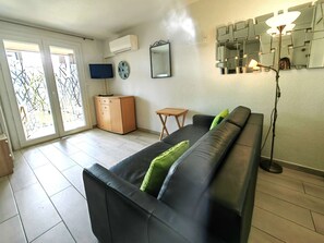 Ein Wohnzimmer mit einer schwarzen Ledersofa, einem Holzkabinett, einem Fernseher, einer Wanduhr, einem Spiegel und einer Stehlampe.