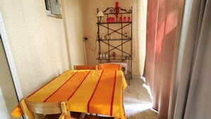 A dining area with a table and chairs, a shelf with various items, and a window with curtains. - Studio cabin, secure parking - 4 guests (Cap d'Agde)