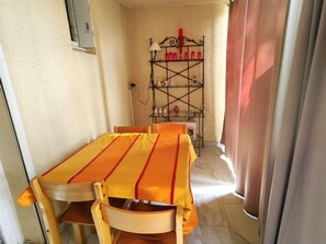 Ein Essbereich mit Tisch und Stühlen, ein Regal mit verschiedenen Gegenständen und ein Fenster mit Vorhängen.