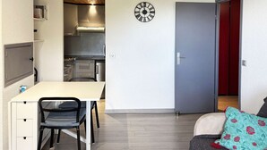 Een ruimtelijk ingerichte leefruimte met kitchenette, een eethoek en een deur naar een rode kamer.