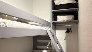 Een stapelbed met een ladder, een plank met opgevouwen kleding en een hangrek met schoenen.