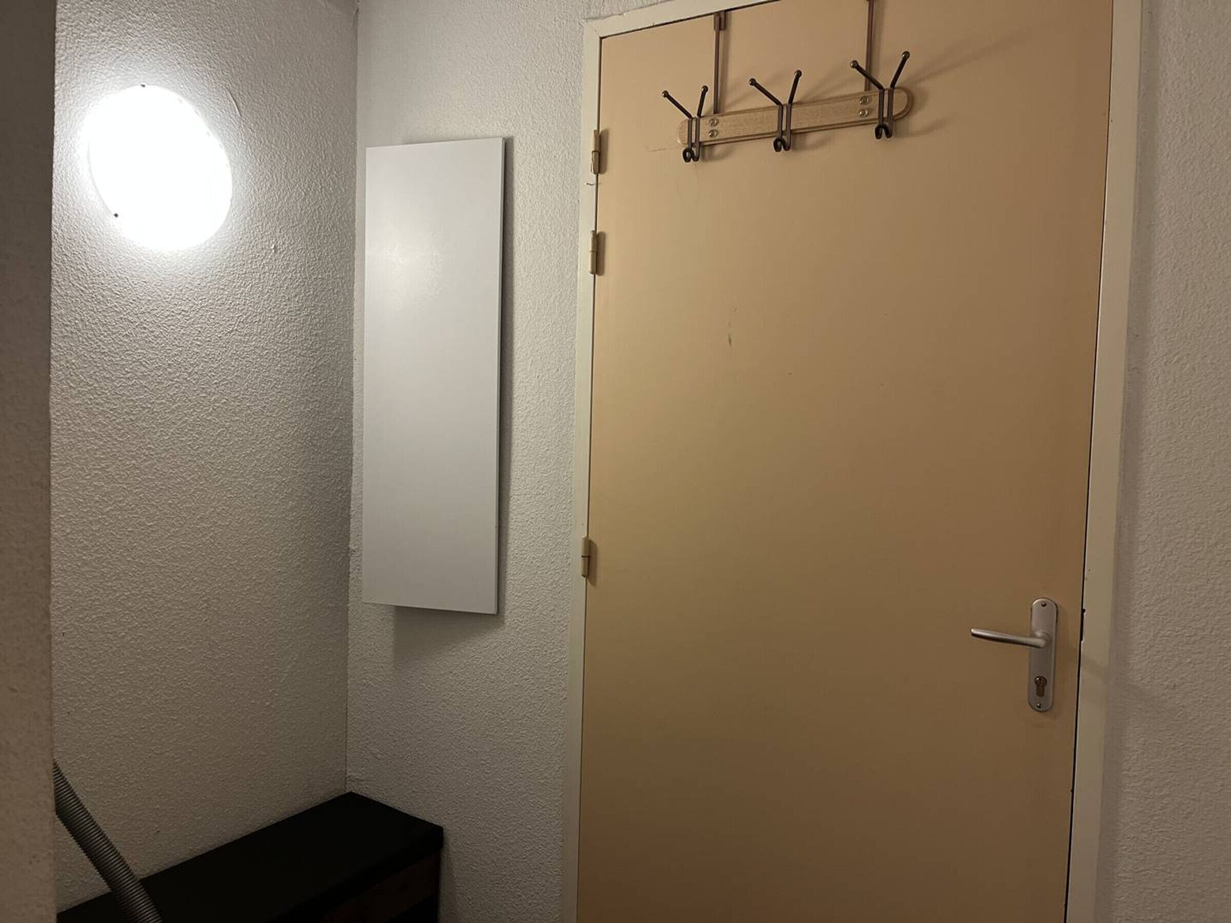 Een kamer met een whiteboard, een deur met een hendel en een kapstok met haken.