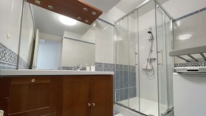 Ein Badezimmer mit Dusche, Waschtisch und Spiegel sowie einem gefliesten Boden.