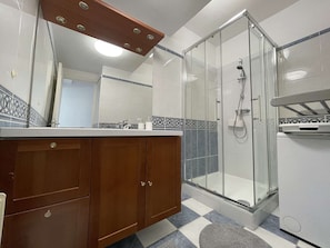 Ein Badezimmer mit Dusche, Waschtisch und Spiegel sowie einem gefliesten Boden.