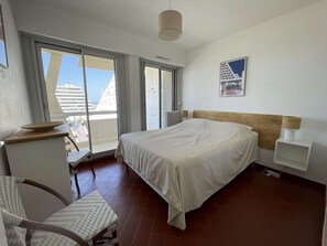 Habitación de hotel con cama, una silla, escritorio, mesita de noche, lámpara y vistas al exterior.