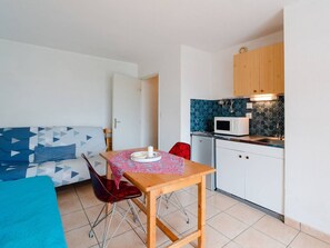Ein kompakter Wohnraum mit Küchenzeile, einer Essecke mit Tisch und Stühlen sowie einer Couch mit gemusterten Kissen.