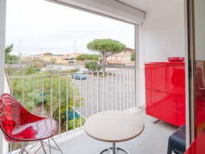 Ein Balkon mit einem roten Stuhl, einem kleinen runden Tisch und einem roten Schrank.