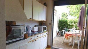 Een keuken met witte kastjes, een magnetron en een broodrooster. Er is een deur die leidt naar een buitenruimte met een tafel en stoelen.