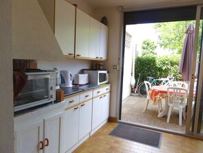 Eine Küche mit weißen Schränken, einer Mikrowelle und einem Toaster. Eine Tür führt zu einem Außenbereich mit Tisch und Stühlen.