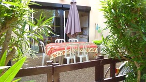 Een terras buiten met een tafel en stoelen, omringd door groen.