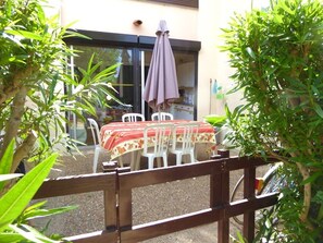 Eine Terrasse im Freien mit Tisch und Stühlen, umgeben von viel Grün.