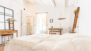 Un dormitorio con una cama grande, un escritorio de madera, una escalera y un ventanal con cortinas.