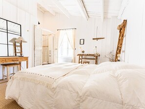 Ein Schlafzimmer mit einem großen Bett, einem Holztisch, einer Leiter und einem Fenster mit Vorhängen.