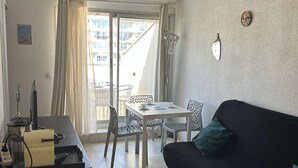 Ein Zimmer mit Esstisch, Stühlen, einer schwarzen Couch, einem Fernseher und einem Fenster mit Vorhängen.