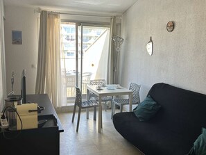 Ein Zimmer mit Esstisch, Stühlen, einer schwarzen Couch, einem Fernseher und einem Fenster mit Vorhängen.